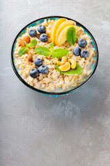 Oatmeal porridge with apple slices and fresh mint. Oatmeal bowl with blueberry and nuts on a gray background. Top view. Copy space