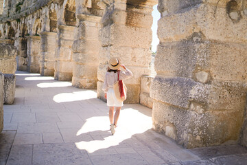 woman in hat stands and looking on Coliseum in Pula Croatia. travel concept.Young woman enjoy summer Italian vacation in Europe. - obrazy, fototapety, plakaty