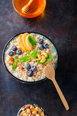 Bowl of oatmeal with blueberry, nuts and honey on a dark background. Oatmeal porridge with apple slices and fresh mint. Healthy food concept. Top view. Copy space
