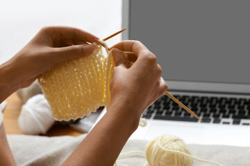 Young African-American woman taking online knitting classes at home, closeup