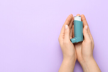 Woman holding asthma inhaler on color background