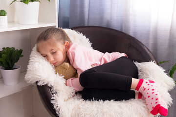 Little girl in a pink T-shirt fell asleep on an armchair hugging a teddy bear. The concept of the...