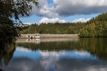 Fototapeta na wymiar dam with blue sky and clouds on a beautiful day in fall with reflections on water