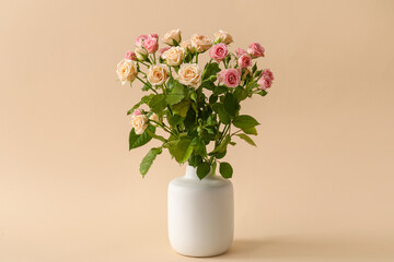 Vase with bouquet of beautiful roses on beige background