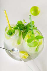 Two mojito glasses with straws. Mojito cocktail with lime and mint on white table. Summer refreshing cocktail and bar accessories on a white plate