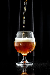 glass of beer on dark background. beer being poured into glass