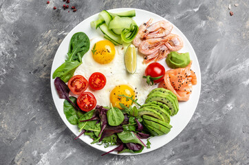 Ketogenic breakfast. Keto low carb salmon, boiled shrimps, prawns, fried eggs, fresh salad, tomatoes, cucumbers and avocado. Top view