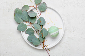 Plate with bath bomb and eucalyptus branches on light background