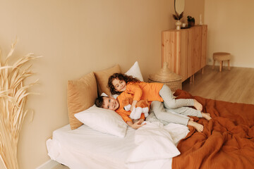 Happy cheerful sleepy children brother and sister in orange bright pajamas have fun laughing and fighting with pillows in a cozy bedroom at home. Children's pajama party. Selective focus