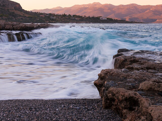 Seascape with blurred waves, rocky beach and sunset mountains, Monemvasia, Greece