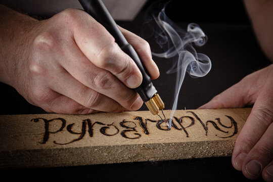 Close-up of hands carefully burning a design into wood with a pyrography pen..