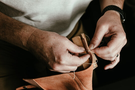 Close up of hands carefully stitching leather.