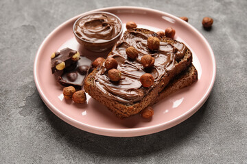 Plate of bread with chocolate paste and hazelnuts on grey background
