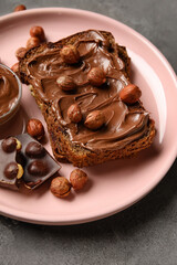 Plate of bread with chocolate paste and hazelnuts on grey background, closeup
