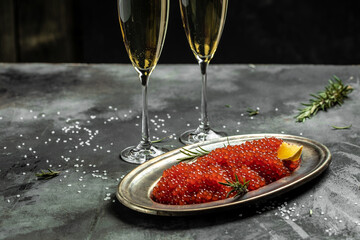 Red caviar filling metal plate and a glass of champagne on a stone background. Gourmet food close up, appetizer, selective focus, place for text