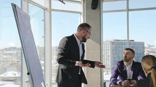 Businessman in suit talking to business people colleagues or partners sitting at conference table. Leader discussing work at morning team meeting.