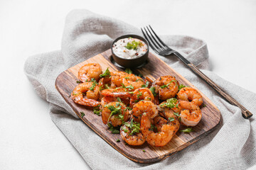 Wooden board of tasty shrimp tails with sauce on white background
