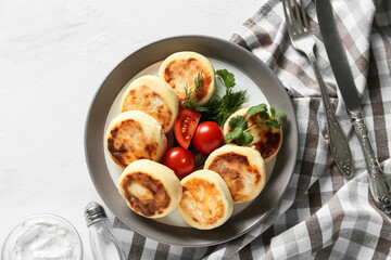 Plate with tasty cottage cheese pancakes and tomato on light background