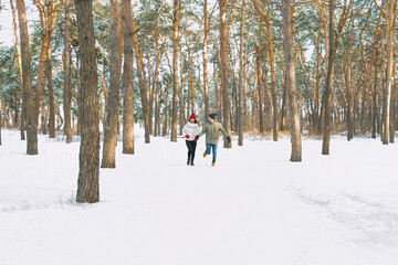 Fototapeta na wymiar Young boy and girl running in winter park. Young couple are running on sunny day in snowy forest.