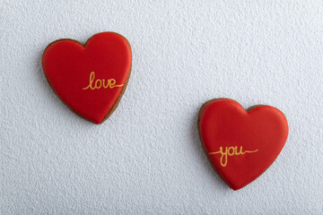 Two heart-shaped cookies with red sugar icing and inscription LOVE YOU, white background