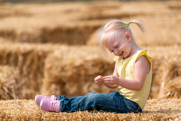 Naklejka na ściany i meble Portrait of cute smiling girl on haystack. Childhood on the farm. Hay harvesting.