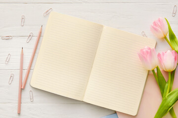 Blank notebook, pencils, clips and tulips on light wooden background