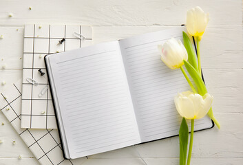 Naklejka premium Notebooks and beautiful tulips on light wooden background