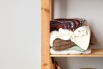 Fototapeta na wymiar Shelving unit with warm sweaters near light wall, closeup