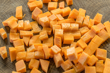 Fresh carrot cubes on a light wooden table.