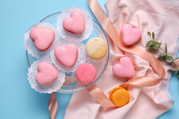 Dessert stand with tasty heart-shaped macaroons on blue background