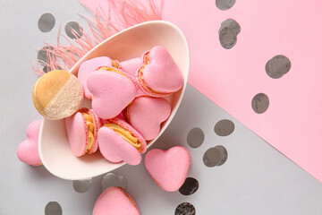 Bowl with tasty heart-shaped macaroons and confetti on color background