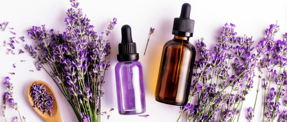 Bottled lavender essential oil and lavender sprigs on white background with copy space, top view....