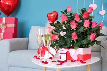 Boxes with engagement ring, glasses of champagne and roses on table in room decorated for Valentine's Day