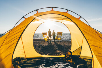 Couple relaxing at camping tent near the sea at sunset.