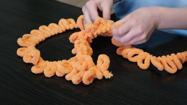 The girl knits with her hands a balaclava of orange color with the help of Alize Puffy threads.