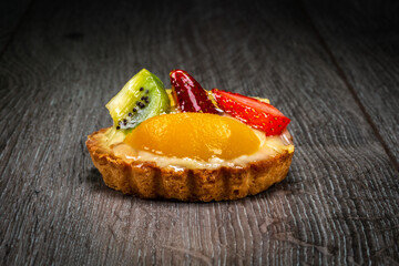 A closeup of a waffle with custard filling decorated with fruits on top on a wooden background dark mode