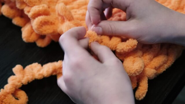 Close-up. The girl knits orange balaclava with her hands using Alize Puffy threads.