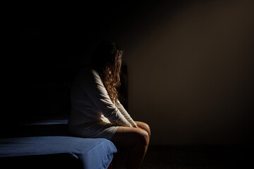 Uma mulher triste, sentada na beirada da cama, de noite. Conceito de depressão.