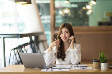 Obraz premium Asian businesswoman talking on the phone and looking at camera.
