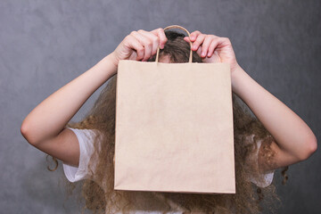 Instead of a face. A girl with curly lush loose hair holding a paper craft bag in front of her face.