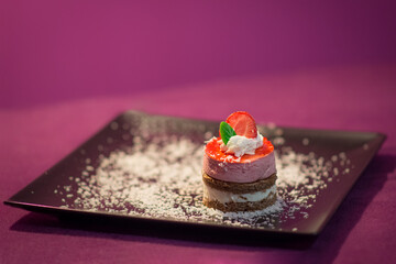 small cake for gourmets, decorated with strawberry and mint, on a black plate