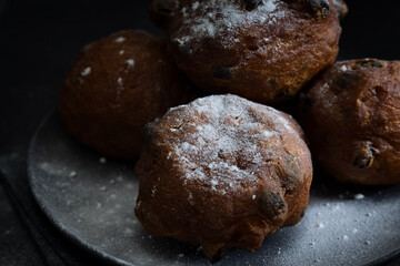 Deep-fried raisins buns. Dutch donuts with raisins and powdered sugar on a plate. Dark moody food photography style with selective focus and copy space, horizontal