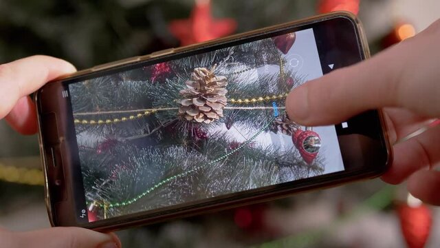 Female Hands are Shooting a Video of Christmas Tree on a Smartphone. Blogger takes pictures, shoots Christmas tree decorations on a mobile phone camera. Preparing New Year. Photographing event. 4K.