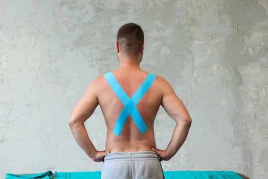 Muscular man with kinesiotaping on the back and shoulders. Kinesiotaping, kinesiology tape - application for back pain.