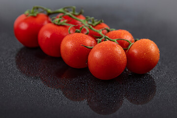Beautiful fresh vine tomatoes (cherry) with drops of water, raw, whole and halved. On black textured slate background. Ingredients of the Mediterranean diet. Top view with copy space. - obrazy, fototapety, plakaty