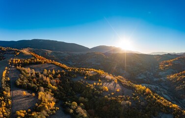 Sun rises above high mountain peaks with yellowed trees