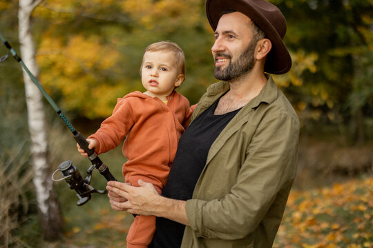 Smiling caucasian man fishing with little son on river or lake coast. Concept of leisure and weekend in nature. Family relationship and spending time together. Warm autumn day