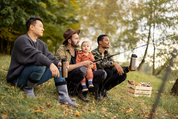 Naklejka na ściany i meble Smiling multiracial male friends resting in nature at autumn. Concept of leisure, weekend and entertaiment. Idea of friendship and spend time together. Caucasian man with fishing rod and little son