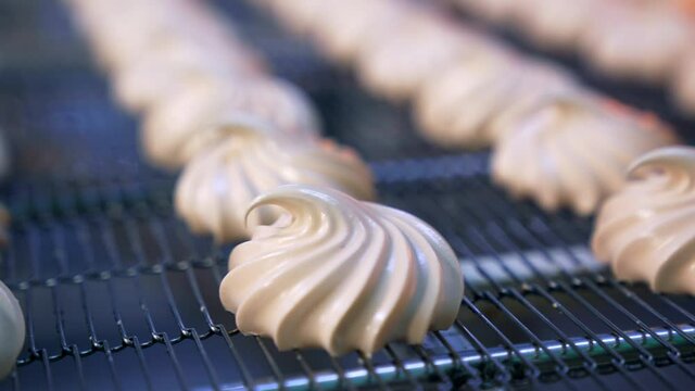 Creamy marshmallows move on the conveyor belt. Savory whipped cream desserts manufactured by modern food factory. Close up. Blurred background.