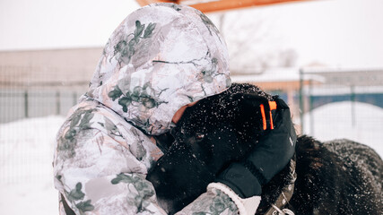 A girl in a colored jumpsuit hugs a black dog with an orange tag in his ear